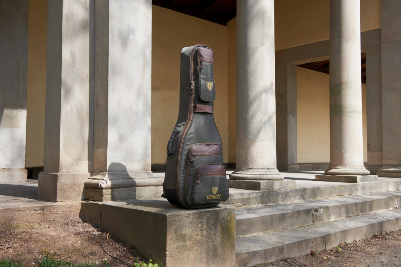 HÉRGÉT guitar case standing on stone steps surrounded by large classical columns in an outdoor colonnade structure.
